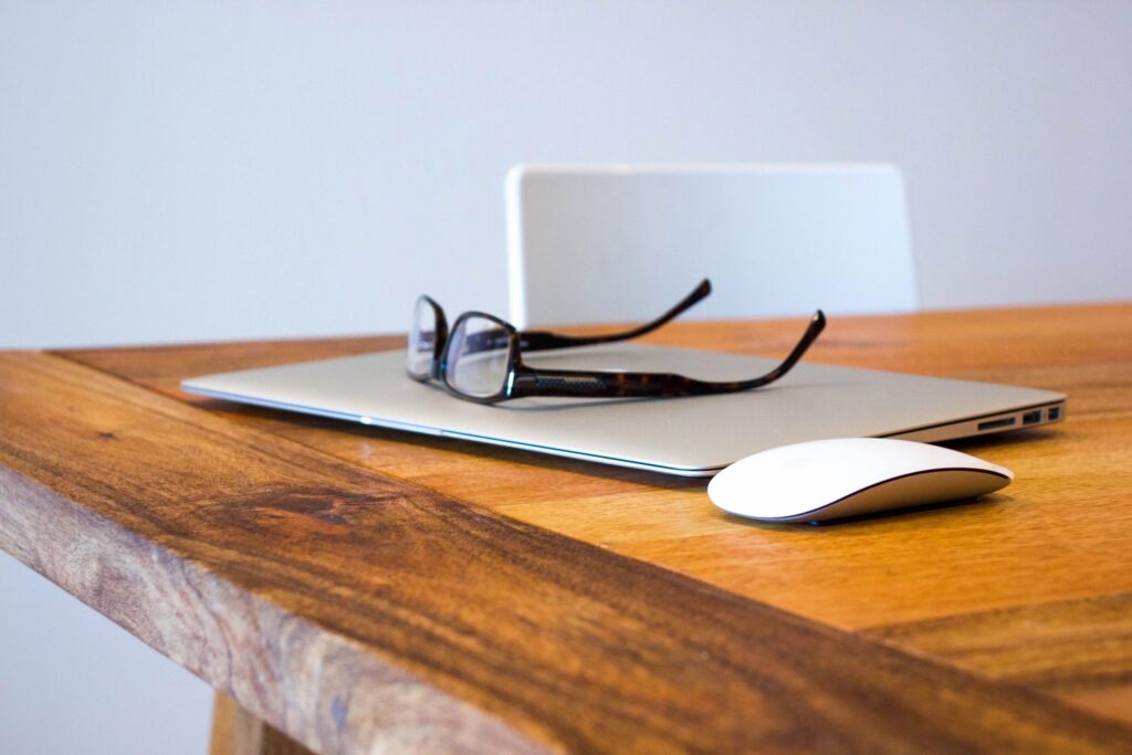 Glasses on laptop with mouse on wooden desk
