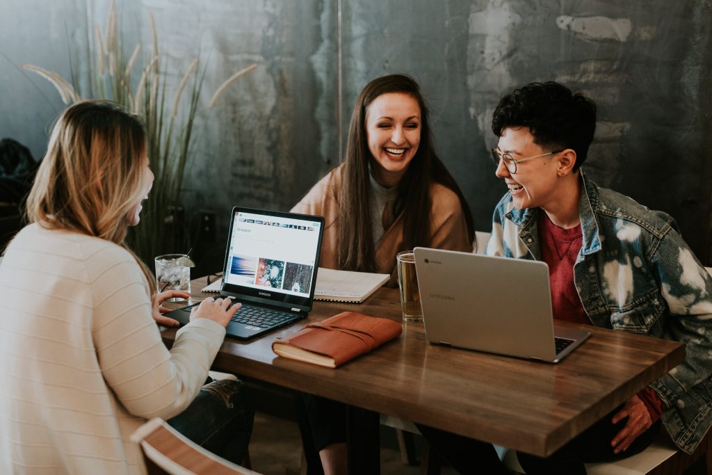 Three friends laughing with laptops at table
