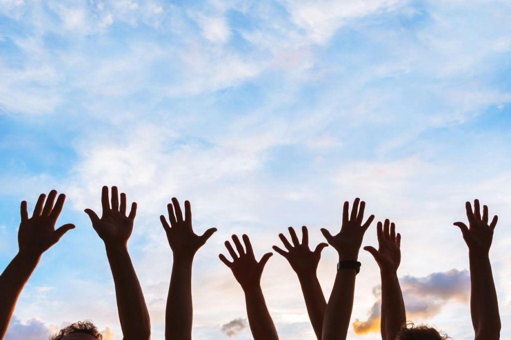 Silhouetted hands raised against blue sunset sky