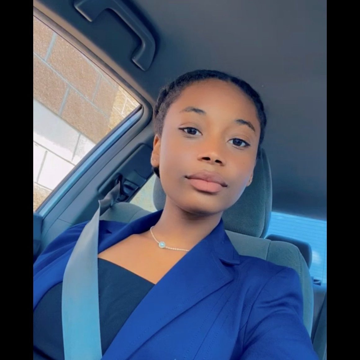Person wearing blue blazer and seatbelt in car